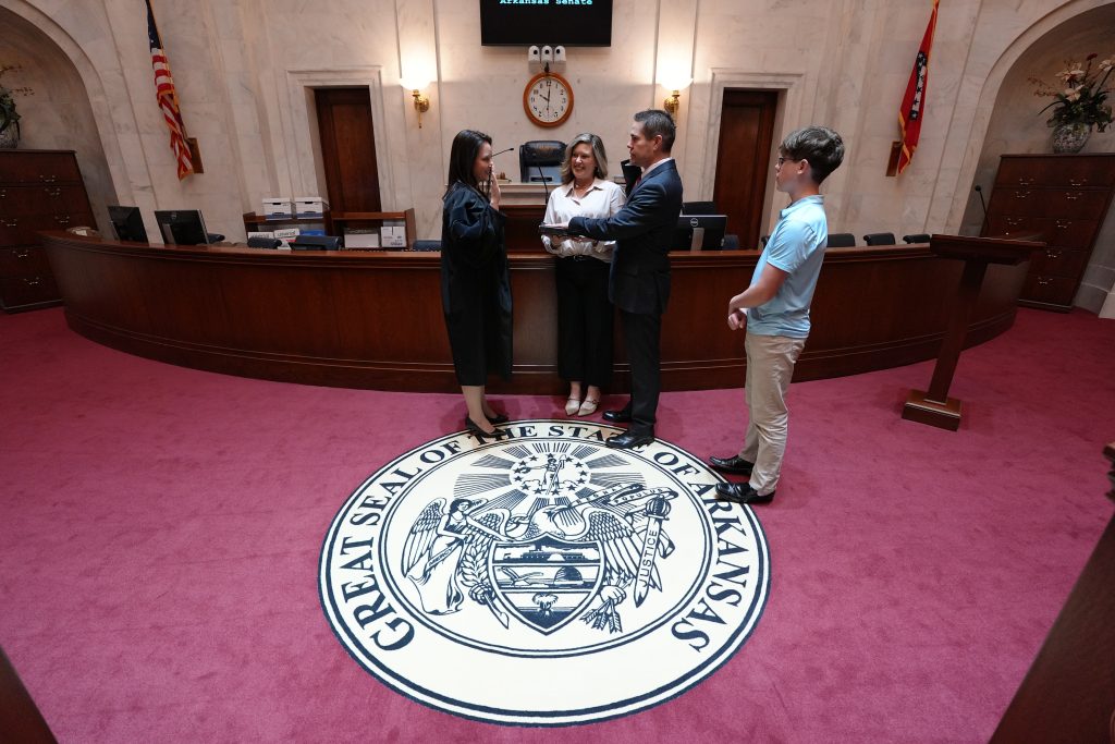 Senator Brad Simon is sworn in as Senator while his wife Stephanie and his son look on. The Great Seal of the State of Arkansas is displayed in the carpet in the foreground.