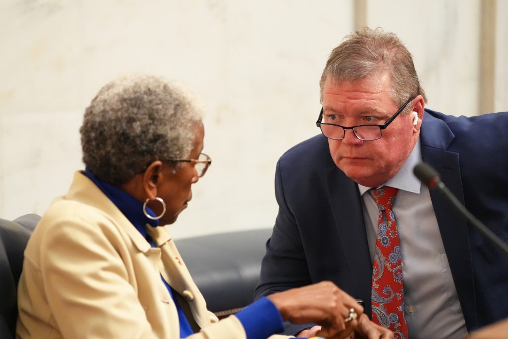 Senator King leans forward in conversation with Senator Flowers in the Senate chamber during a business meeting.