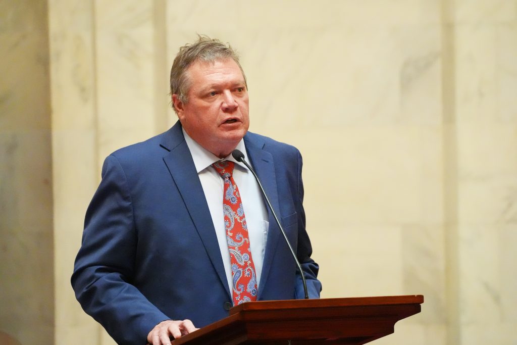 Senator King speaks in the Well in the Senate chamber during a business meeting. He is wearing a blue suit with a red paisley patterned tie.