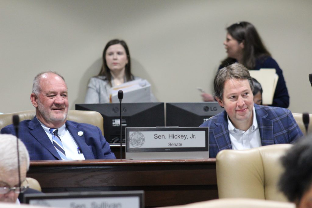 Senator Hickey and Senator Tucker listen and smile during a committee meeting