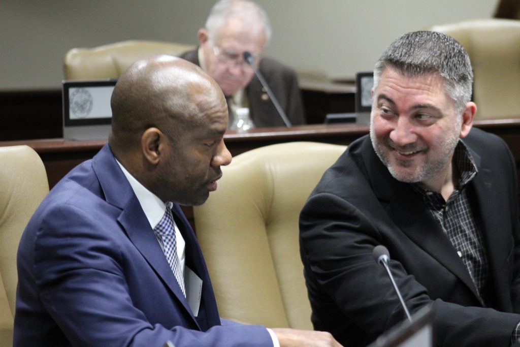 Senators Penzo and Love converse in a committee room.