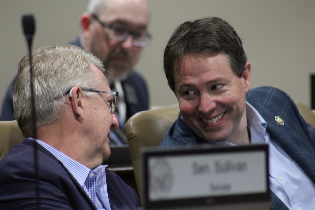 Senator Tucker smiles while talking with Senator Hill during a committee meeting