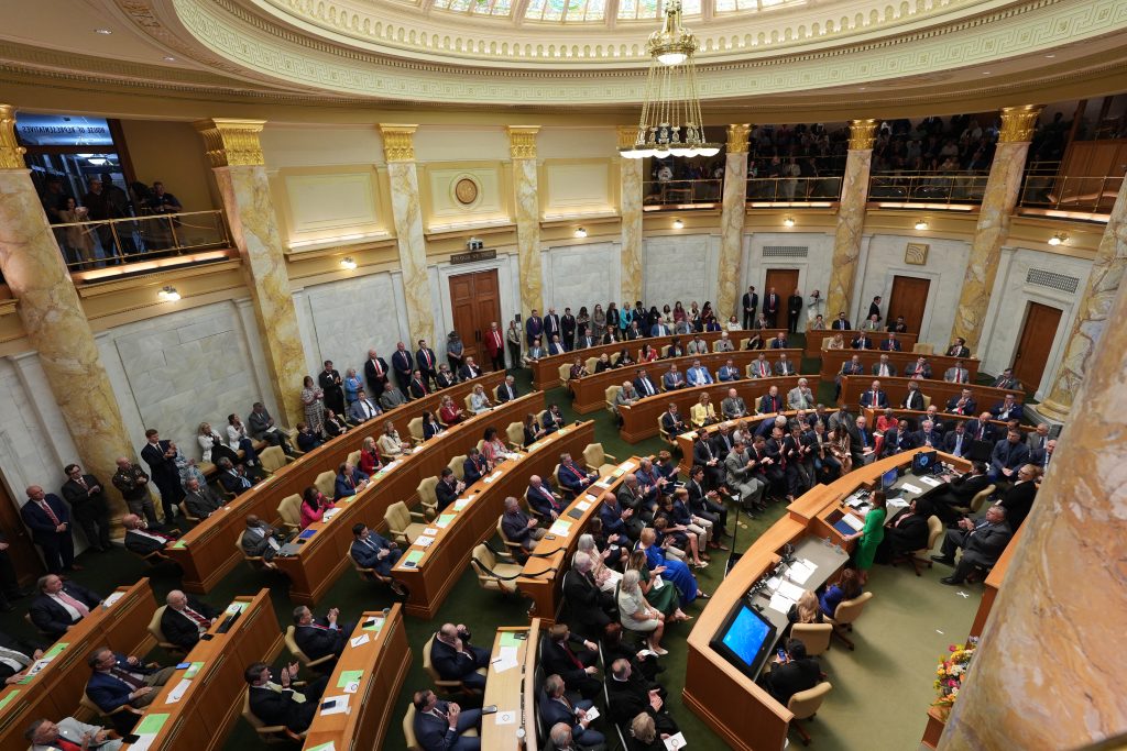 Wide overhead shot of Governor Sanders, wearing a green dress, speaking to the combined Arkansas General Assembly in the House chamber on April 8, 2026