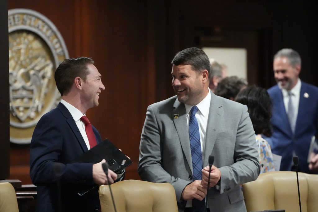 Senator Bart Hester smiles while talking with Senator Tyler Dees in a committee room.