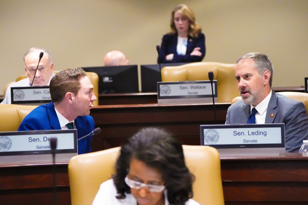 Senators Dees and Leding talk at their desks in a committee room