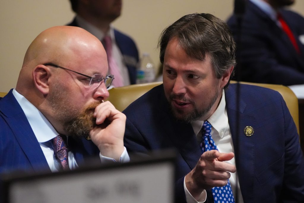 Senators Crowell and Tucker lean in while talking in a committee room. Sen. Tucker is gesturing as he talks.