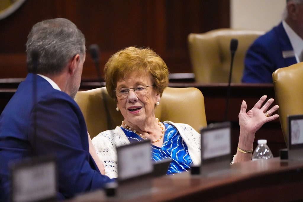 Senator English gestures while speaking with a colleague in a committee room