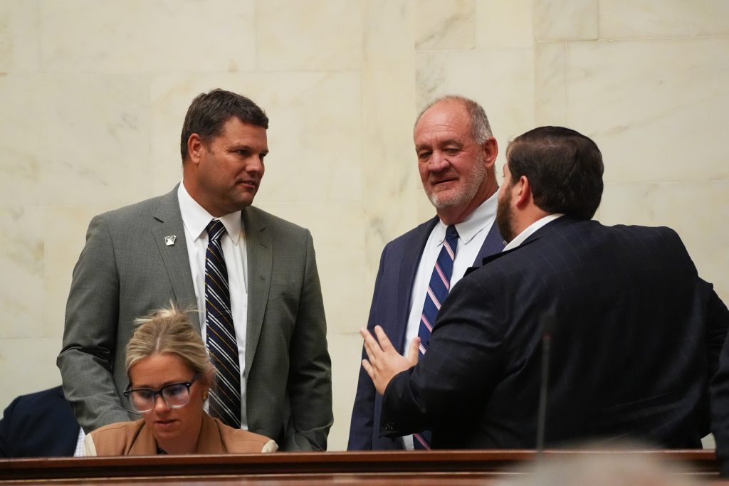 Senators Hester, Hickey, and Gilmore talk in the Senate chamber. Senator Davis can be seen sitting in front of them.