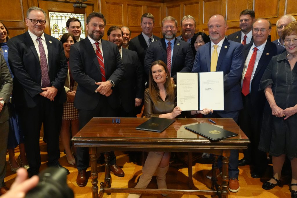 Senators and House members flank Gov. Sanders as she holds up the freshly signed tax bill.