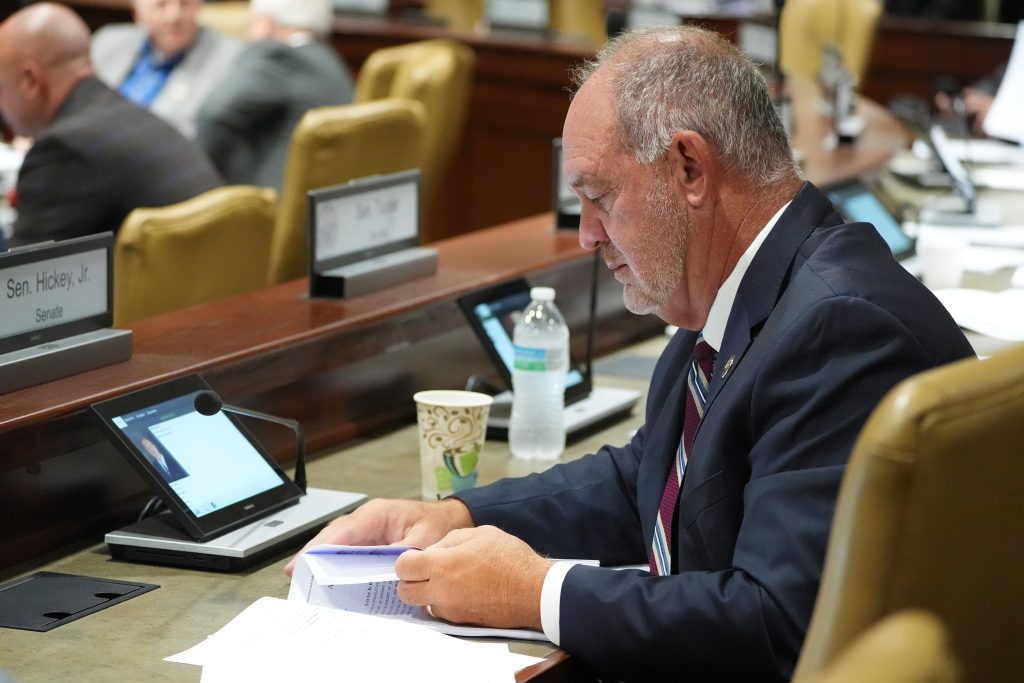 Senator Hickey thumbs through paperwork on his desk in a committee room.