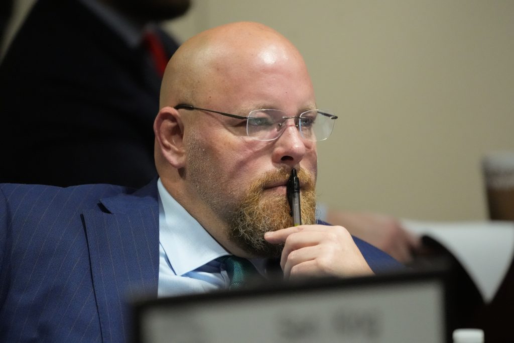 Senator Crowell has a pen to his mouth as he listens to testimony in a committee room