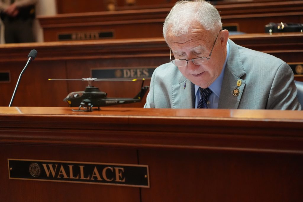 Sen Wallace works at his desk in the Senate chamber. A model Army helicopter is on the ledge in front of him.