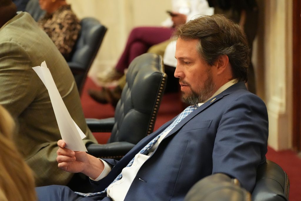 Senator Tucker leans back and reads some papers at his desk in the Senate chamber.
