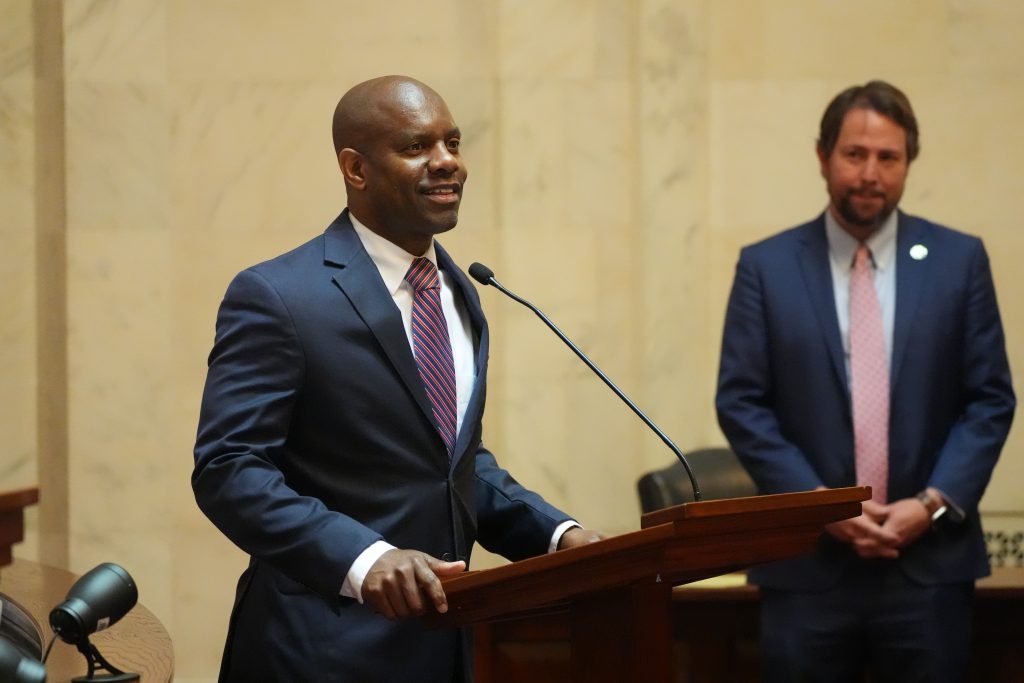 Senator Love speaks from the Well in the Senate chamber as Senator Tucker looks on in the background.