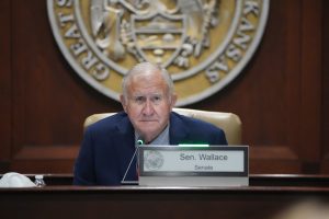 Senator Wallace listens to testimony in a committee room. The Great Seal of Arkansas is on the wall behind him.