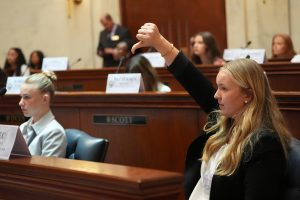 A Girls State delegate gives a thumbs down gesture while sitting in the Senate chamber