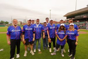 Senators softball team and the Lt. Gov pose at Dickey-Stephens Park, wearing their softball jerseys